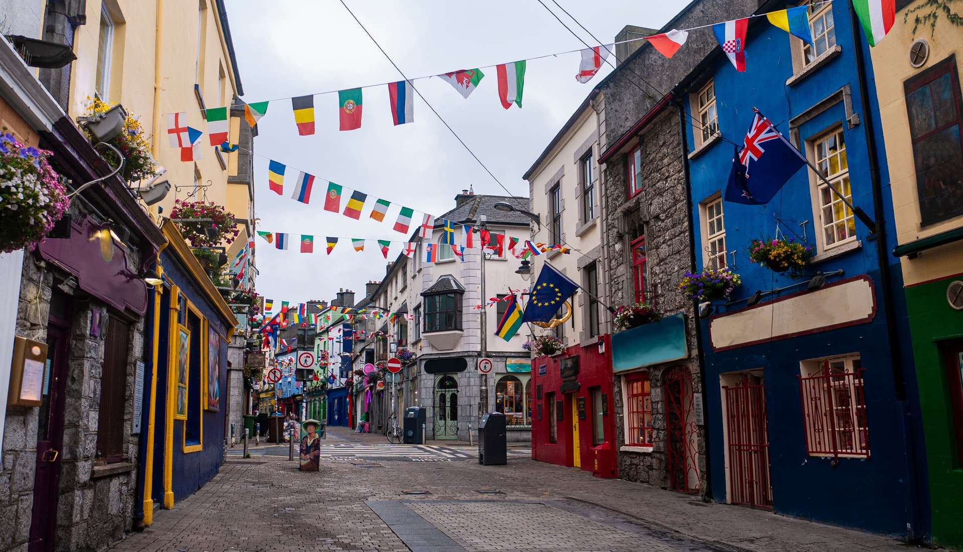Cobblestone street in Galway lined with colorful buildings and international flags strung overhead.