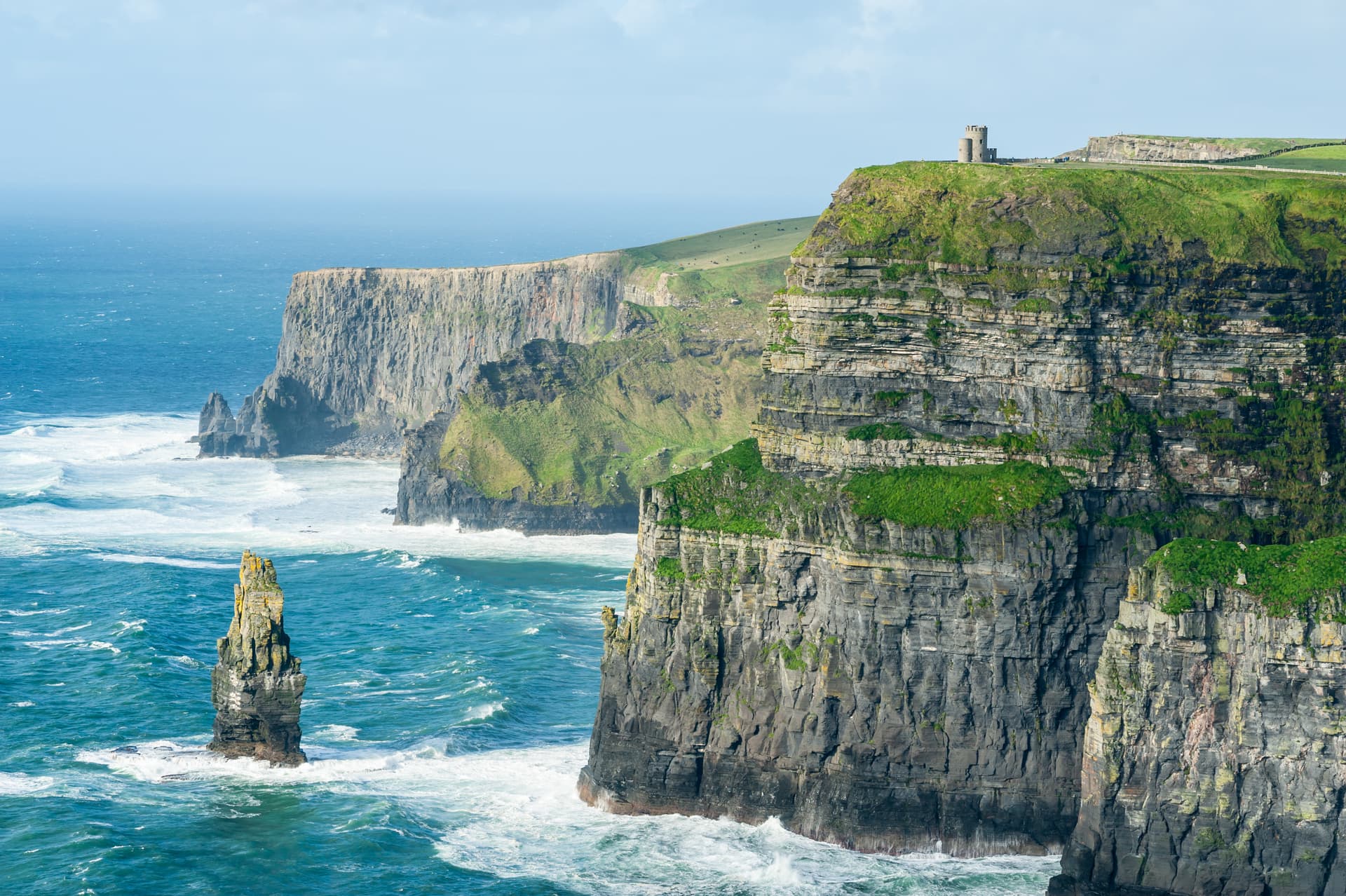 Cliffs of Moher with O'Brien's Tower atop green cliffs overlooking rough blue sea.