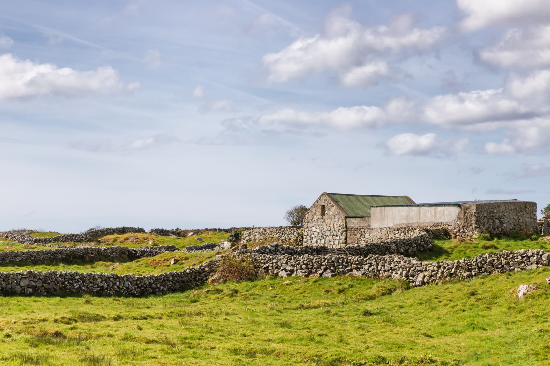 Stone farm building with green roof surrounded by dry stone walls in grassy landscape near Spiddal.