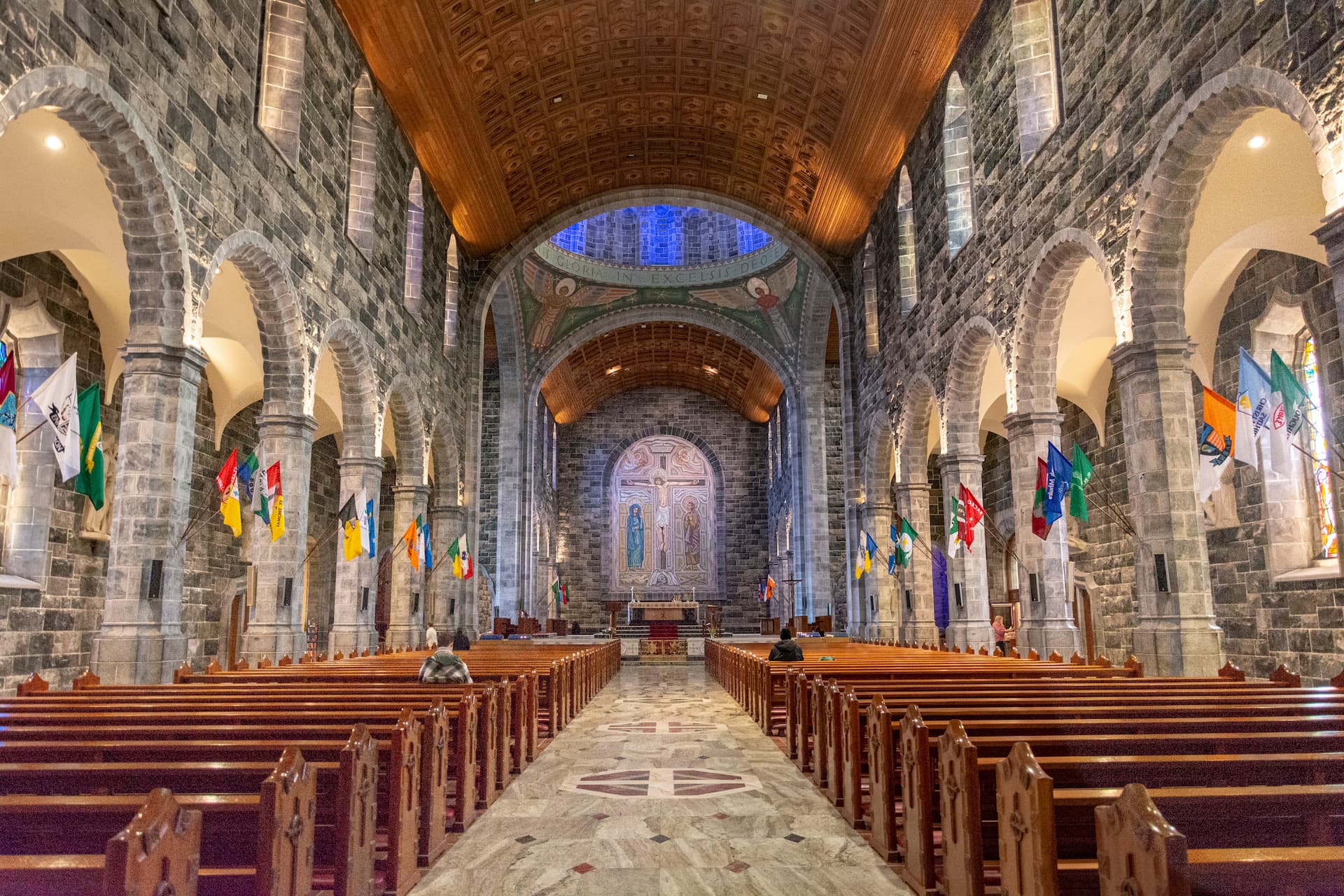 Interior of Galway Cathedral showing stone arches, wooden pews, and flags lining the nave.
