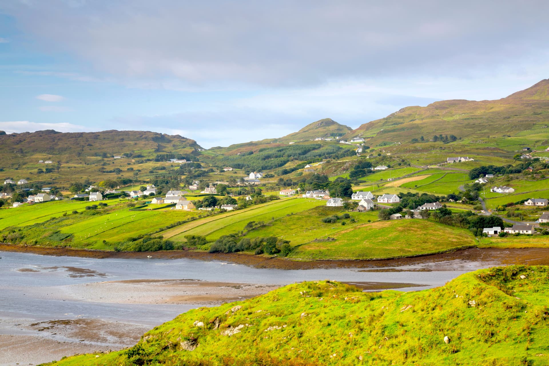 Coastal village with white houses nestled in green hills above tidal flats in Carrick, Donegal.