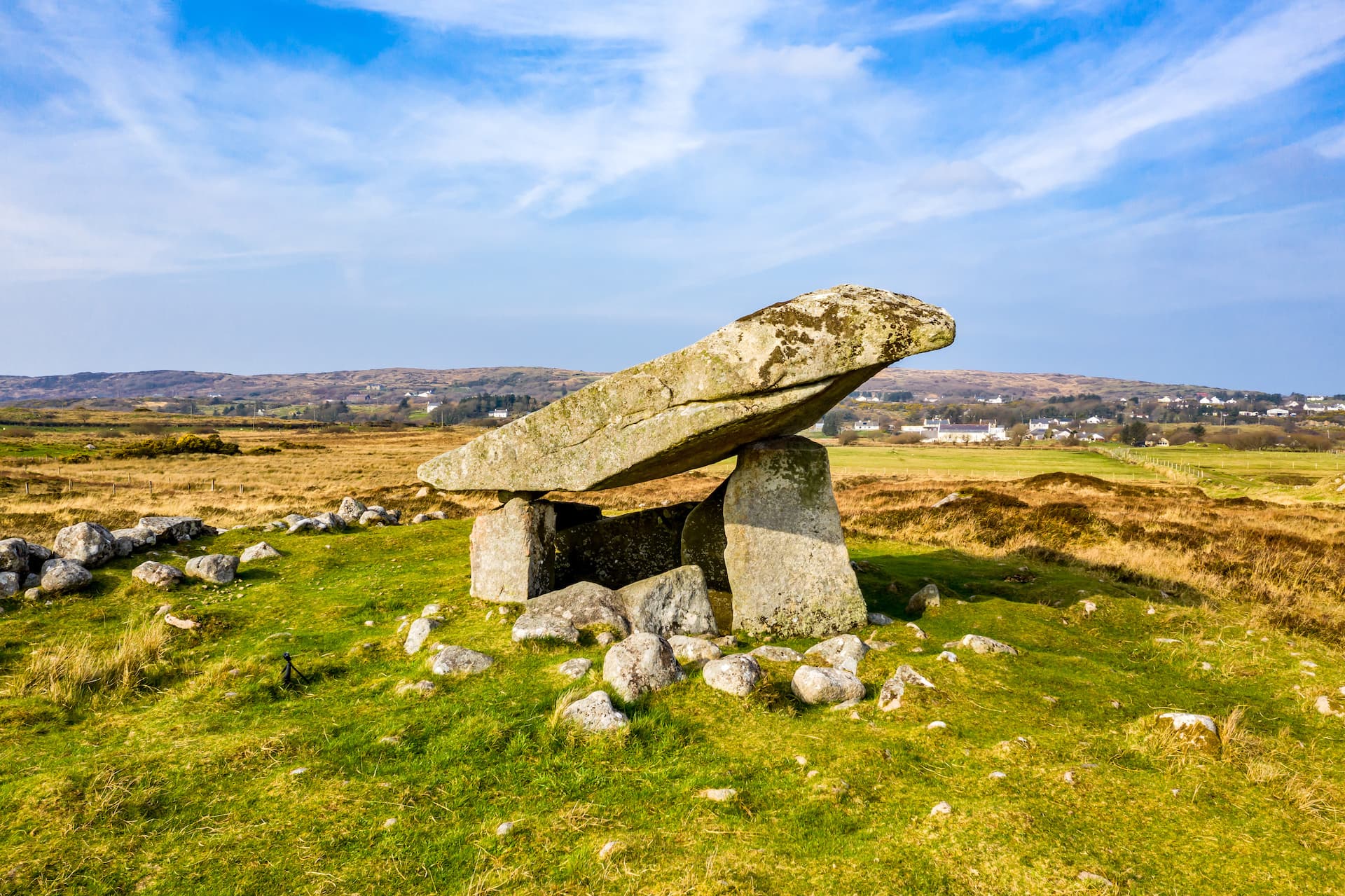 Kilclooney Dolmen megalithic tomb on green grass with rolling hills and village in background.