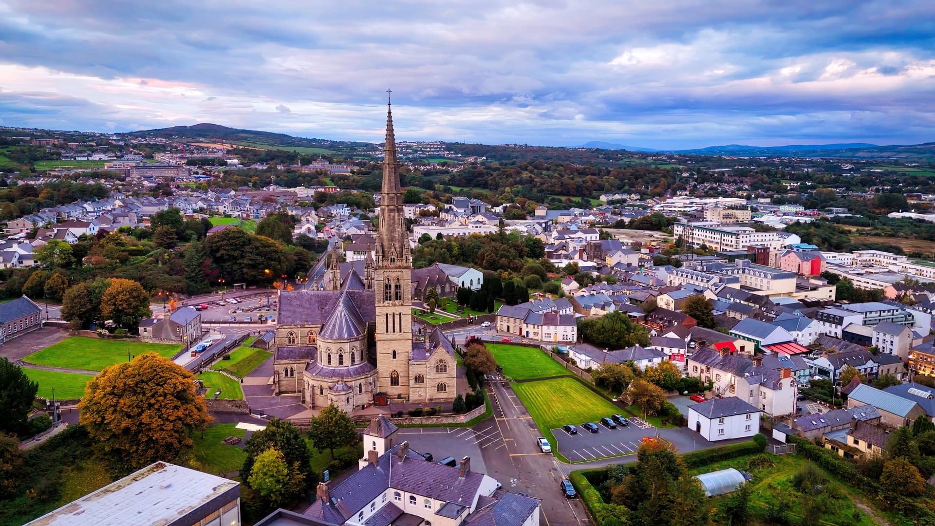 Aerial view of Letterkenny town featuring a large stone church spire surrounded by buildings and green hills.