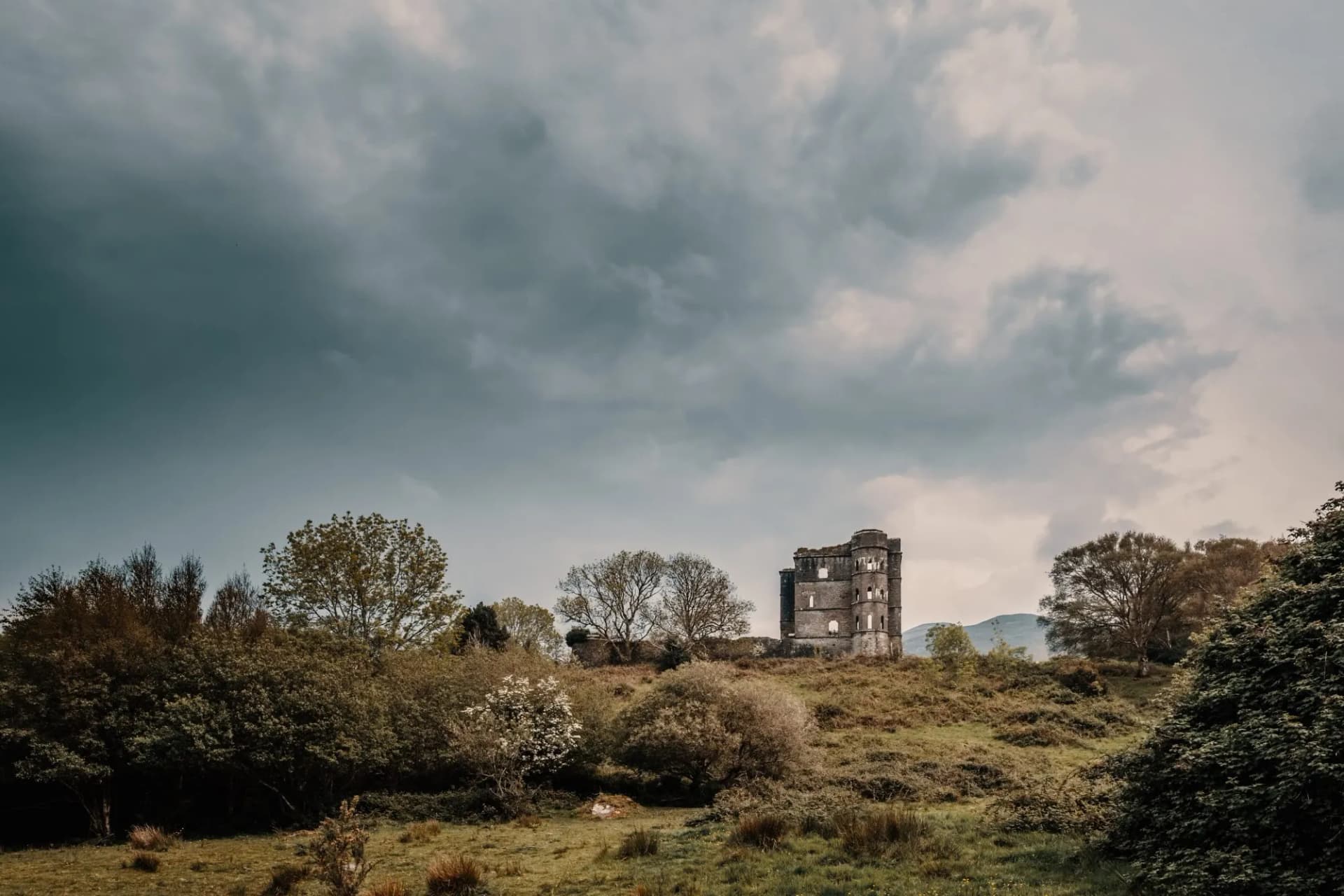 Ruins of Glenbeigh Tower on a grassy hill under dramatic, cloudy sky.