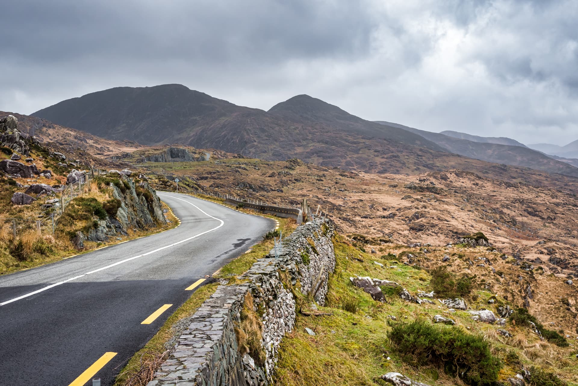 Winding mountain road next to a stone wall under a gray, cloudy sky at Moll's Gap.