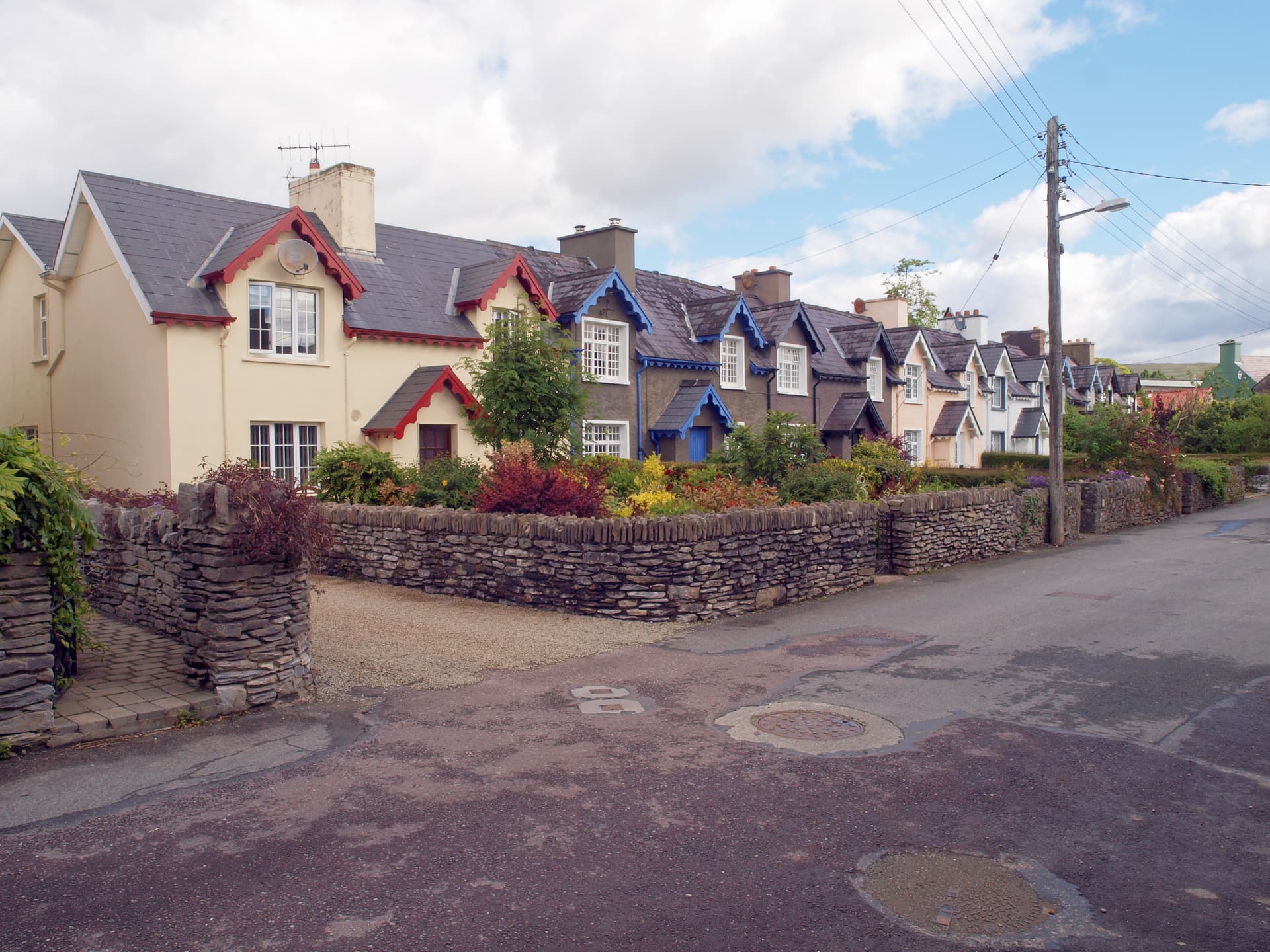 Row of colorful cottages with stone walls and gardens along a street in Kenmare.