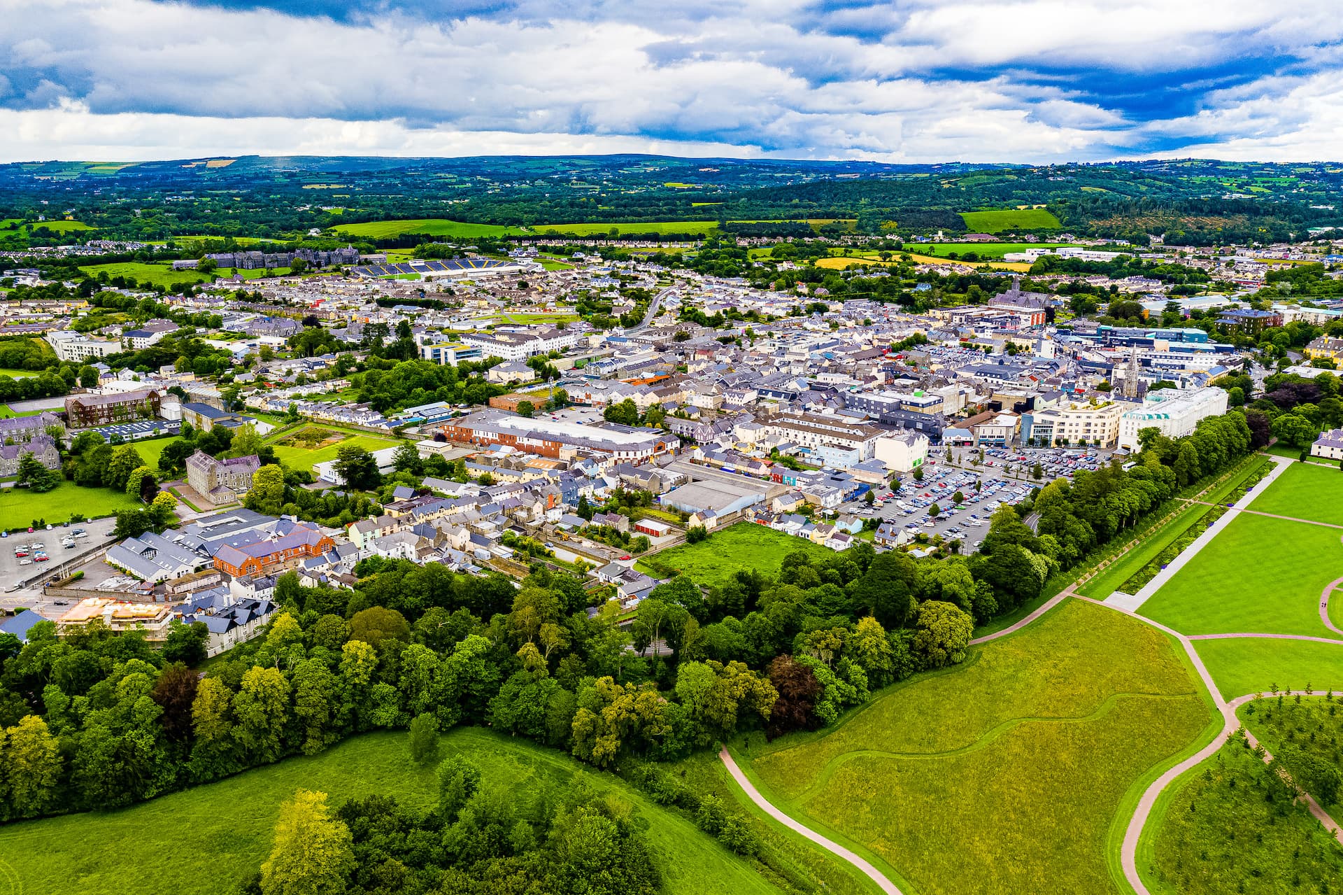 Aerial view of Killarney town surrounded by green fields and rolling hills under a cloudy sky.