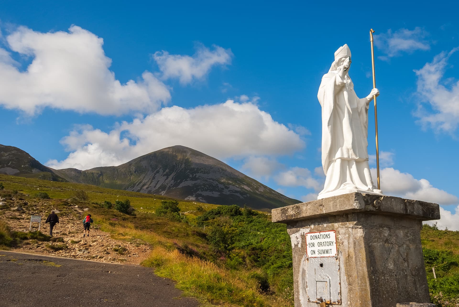 Statue of St. Patrick with Croagh Patrick mountain and hikers on a sunny day.