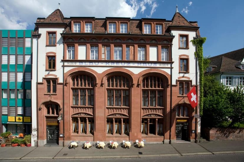 Hotel Blau Kreuz Haus building with Swiss flag, next to modern green building in Basel