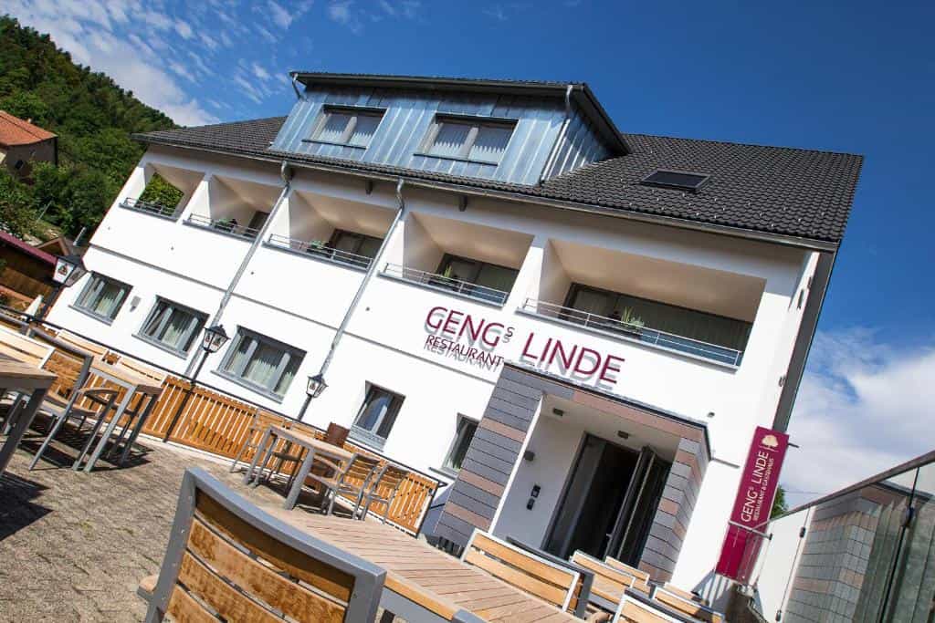 Hotel Gengs Linde restaurant exterior with outdoor seating and forested hill under blue sky.
