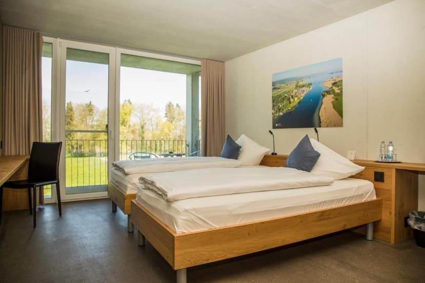 Twin beds in hotel room with balcony view of green lawn and trees, Schaffhausen.