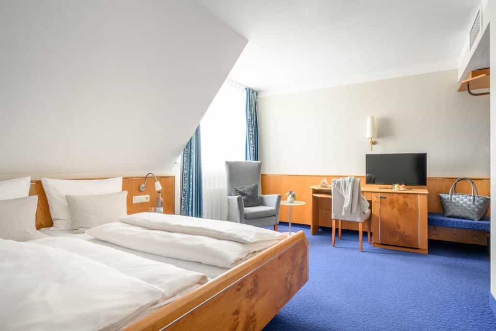 Hotel room with wooden bed frame, blue carpet, and sloped ceiling in Constance.
