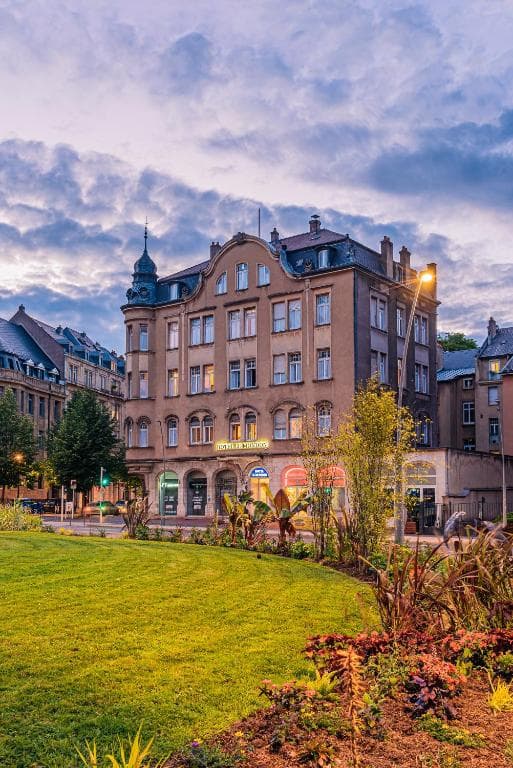 Historic hotel building facade viewed across a green park at dusk in Metz, France.