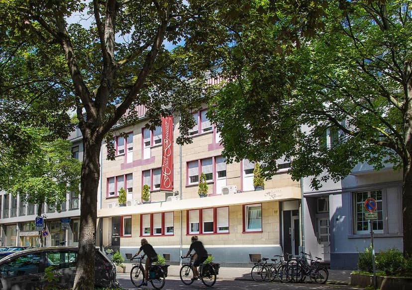 Two people cycling past Hotel Brenner in Koblenz on a sunny day.