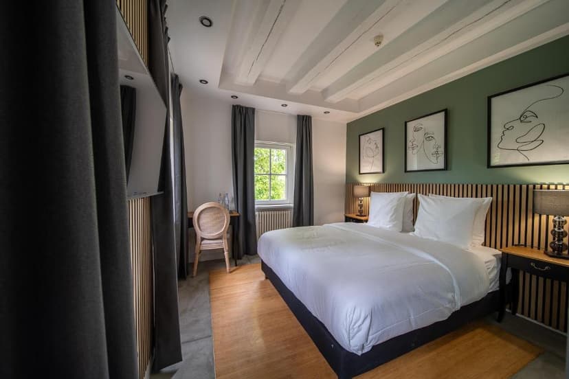Hotel room with white bedding, green accent wall, and modern line art above the bed.