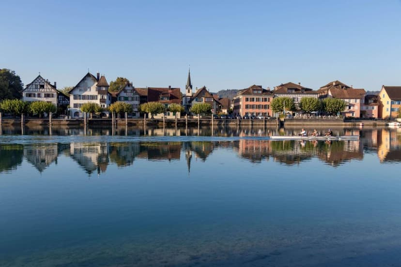 Rowing boat on water with reflection of Kreuzlingen town buildings and church spire.