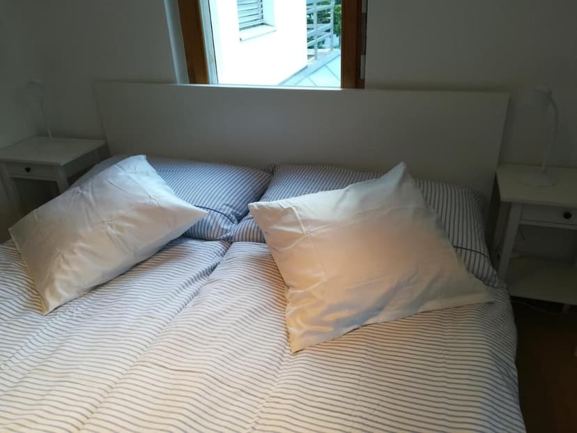 Bedroom with white headboard, striped duvet, white pillows, and window view in Chur Bed & Breakfast.