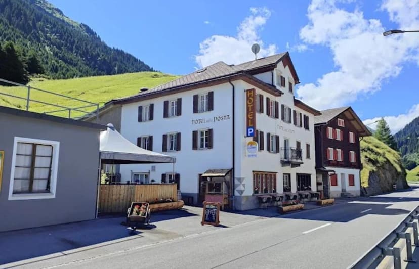 Hotel Dalla Posta in Disentis with white facade, alpine setting, and green mountains.