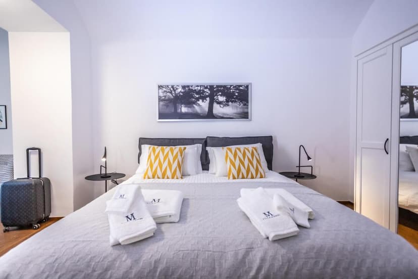 Bedroom in Lucarno Villa Muralto with large bed, yellow pillows, and luggage nearby.