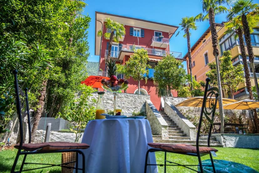 Outdoor breakfast table with fruit and juice set on lawn before red building in Lucarno-Villa Muralto.