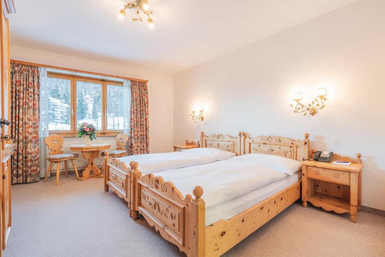 Twin beds with carved wooden frames in a hotel room overlooking a snowy alpine scene.