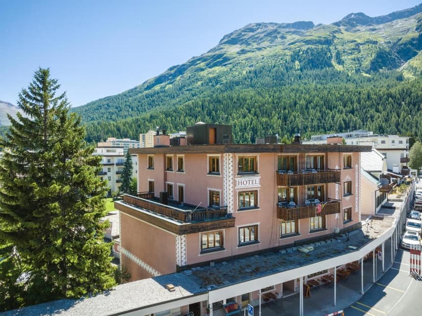 Hotel Corvatsch building in St. Moritz with a forested mountain backdrop under a clear sky.