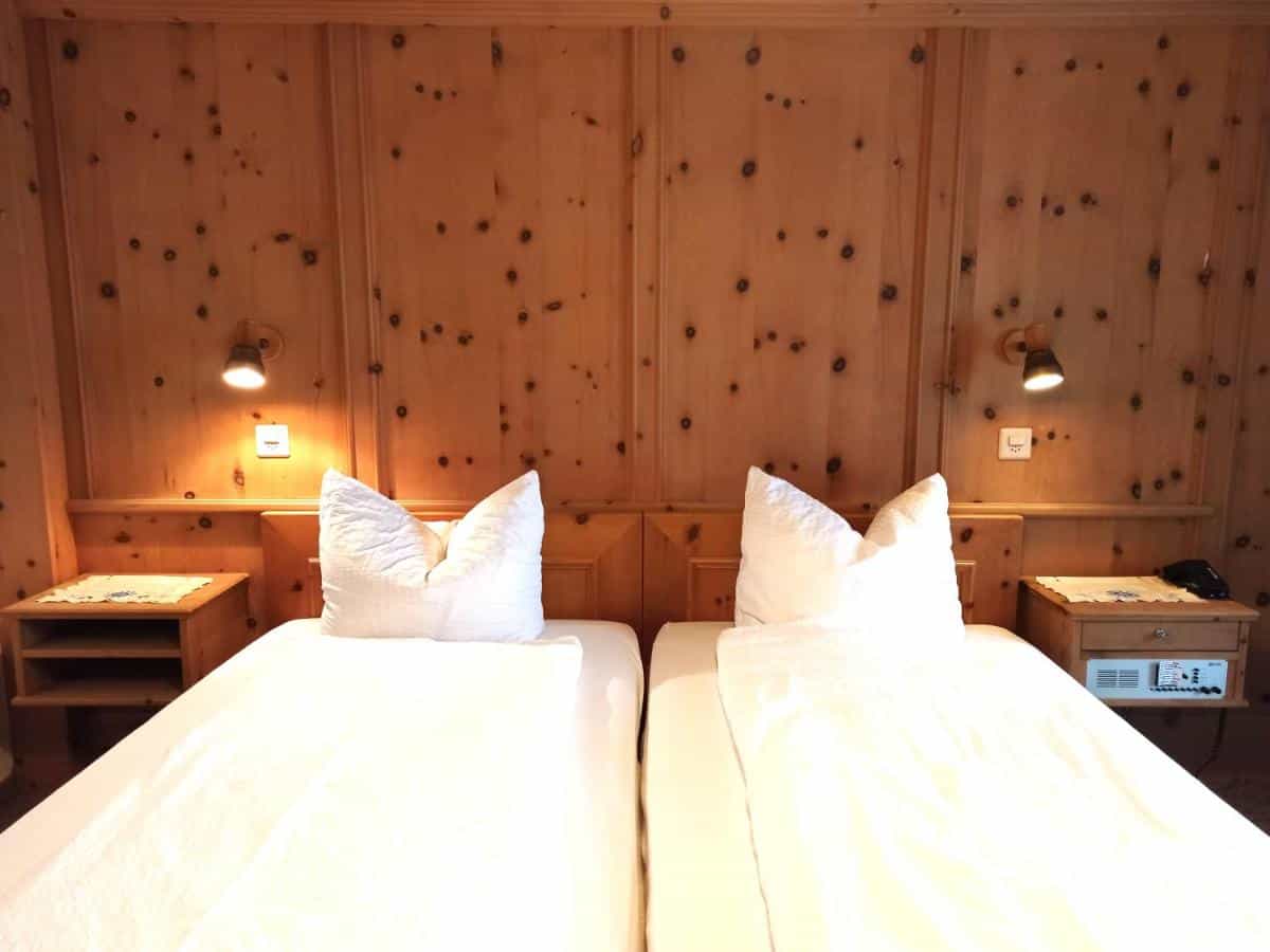 Twin beds with white linens against knotty pine wood paneling in a Hotel Acla Fili room in Zernez.