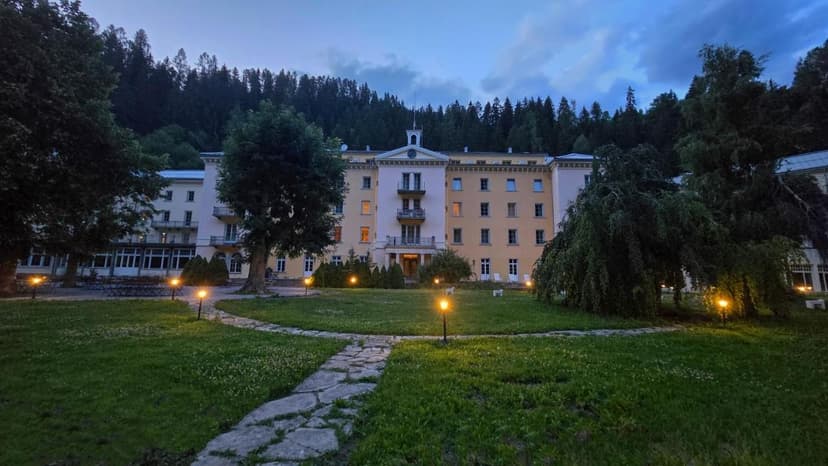 Scuol Palace hotel illuminated at dusk with lawn and forest background