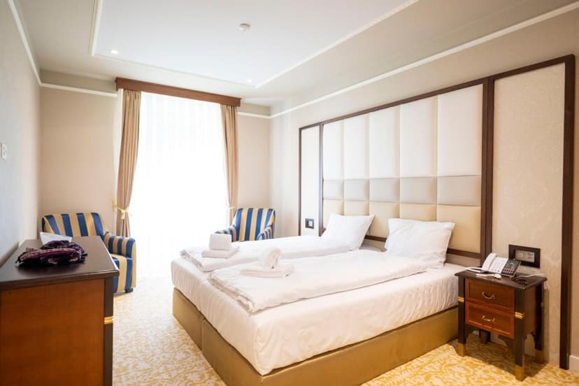 Twin beds with white linens in a hotel room at Scuol Palace with striped armchairs.
