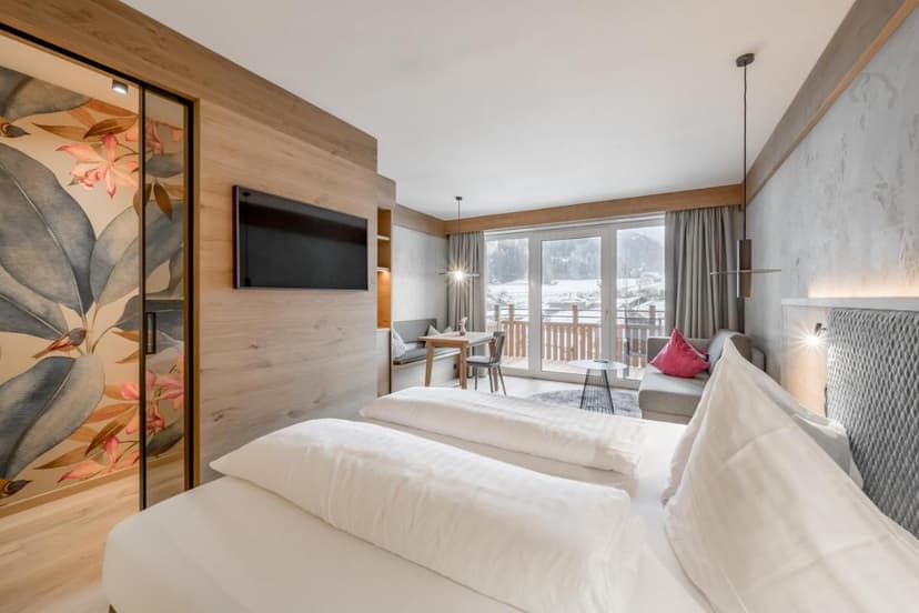 Modern hotel room with twin beds, wood paneling, and balcony view of snowy landscape in Prutz.
