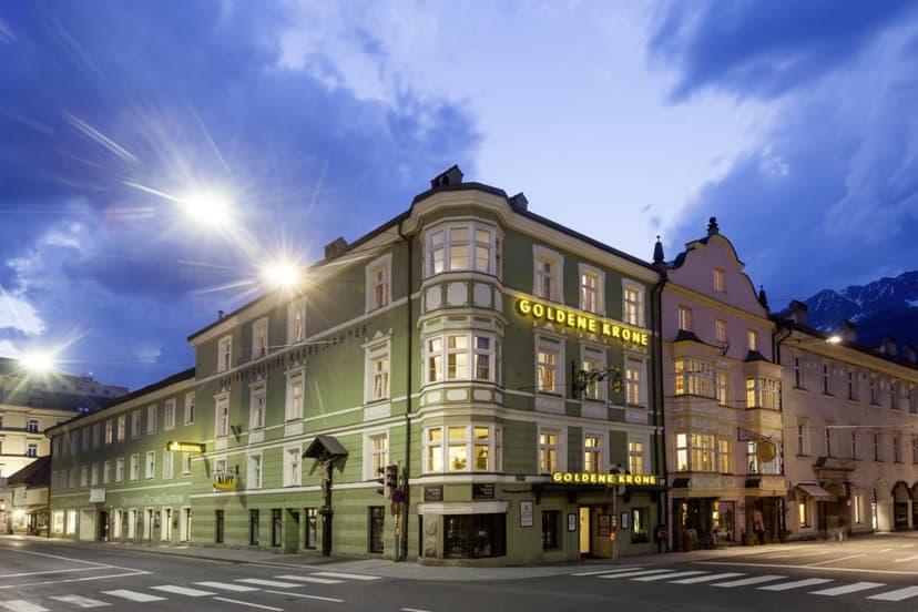Hotel Goldene Krone building illuminated at dusk in Innsbruck with mountains visible.