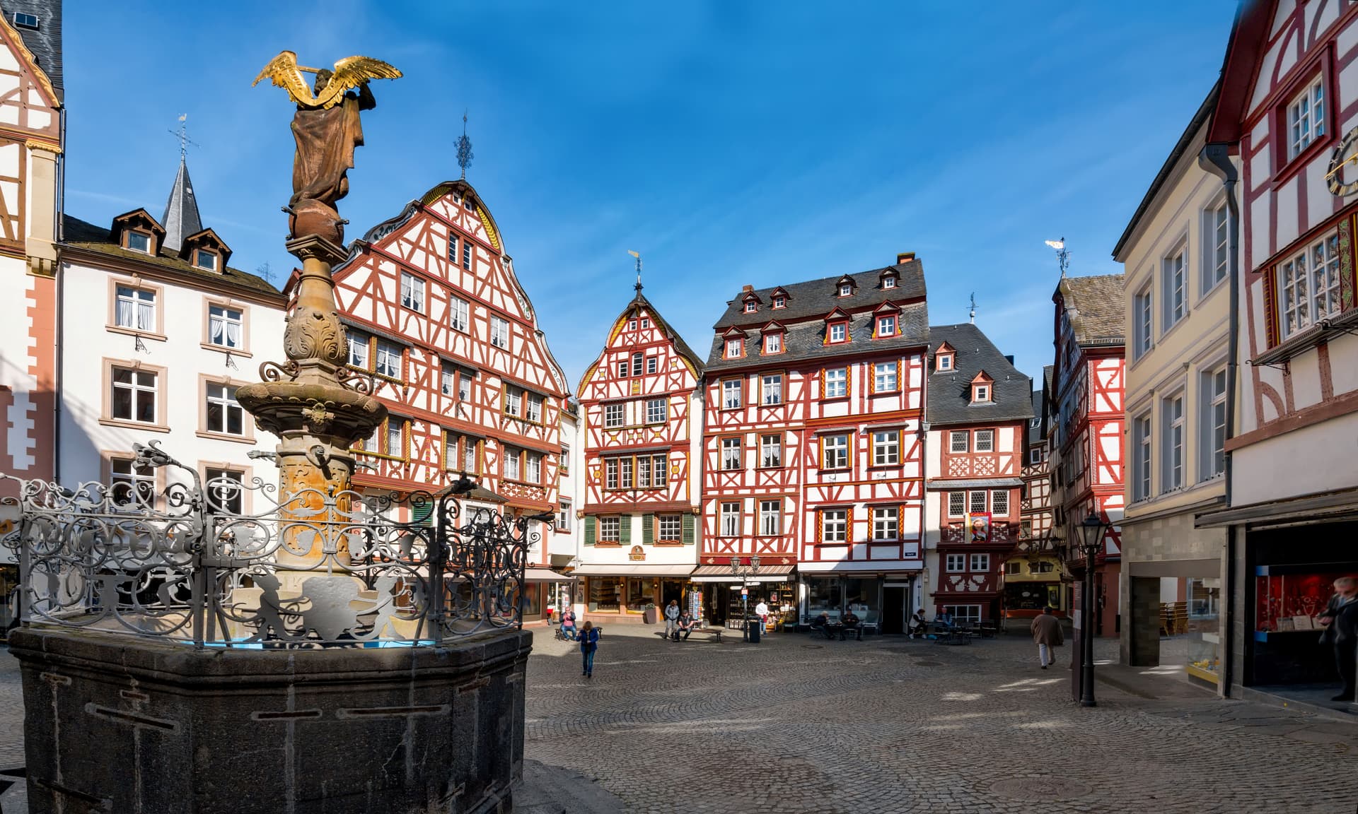 Fountain with golden angel statue in cobblestone square surrounded by half-timbered buildings.