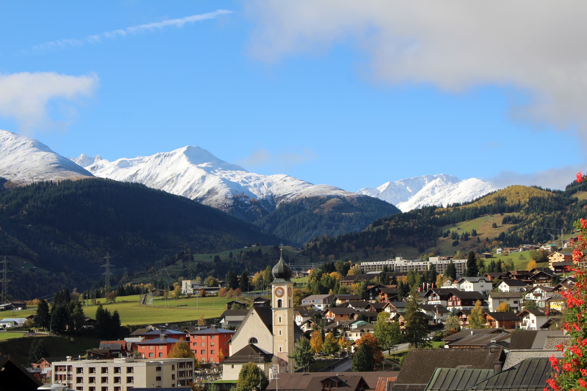 Parish church in Disentis with village houses below snow-capped alpine mountains.