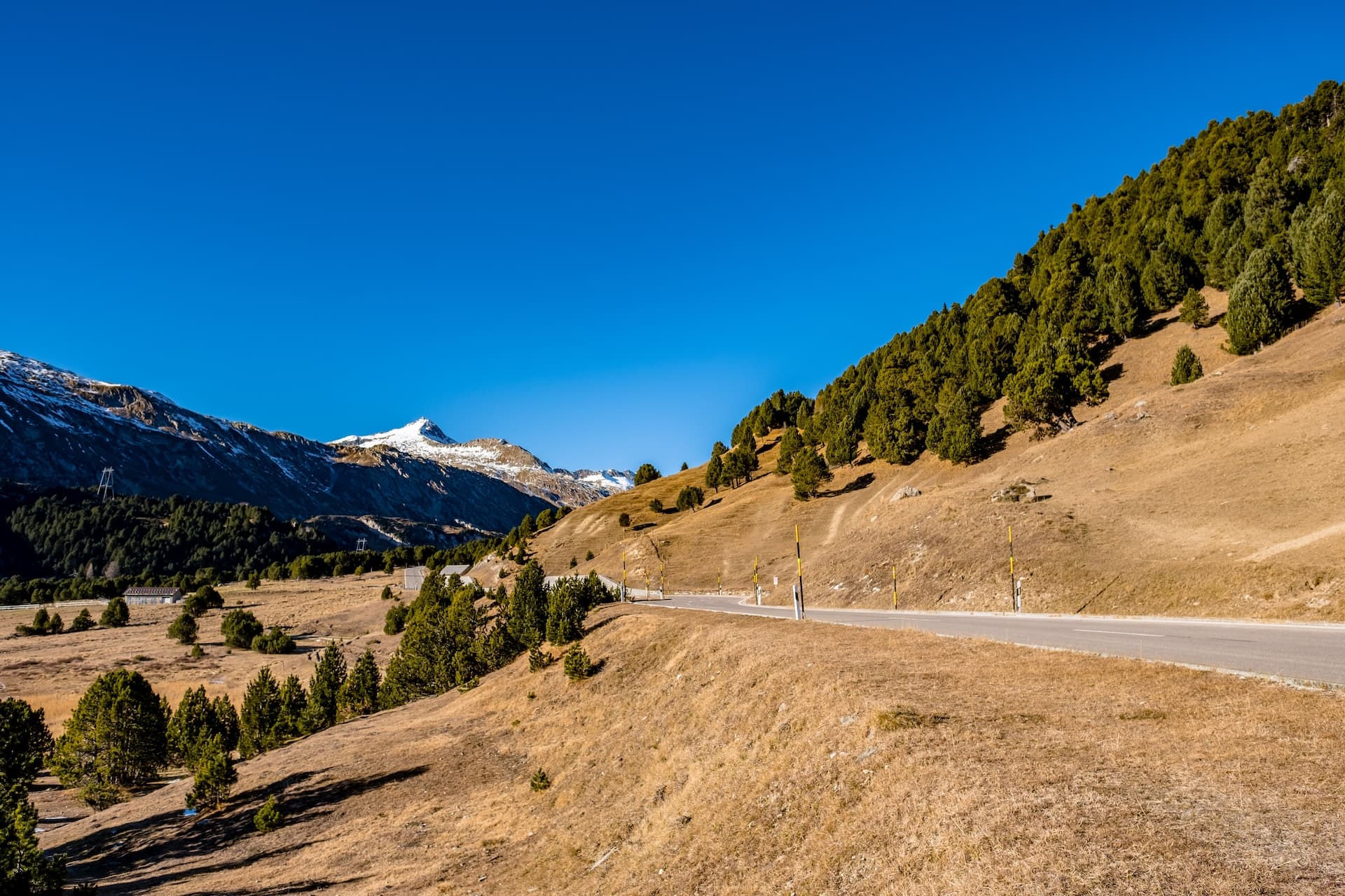 Mountain road through dry alpine landscape with snow-capped peaks at Lukmanier Pass, Switzerland.