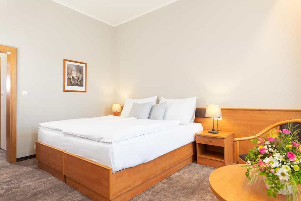 Hotel room with wooden bed frame, white linens, bedside lamps, and a floral arrangement.