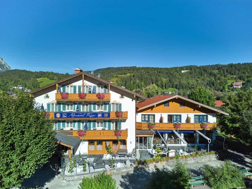 Alpenhotel Rieger in Wallgau with balconies and outdoor seating against a backdrop of green mountains.