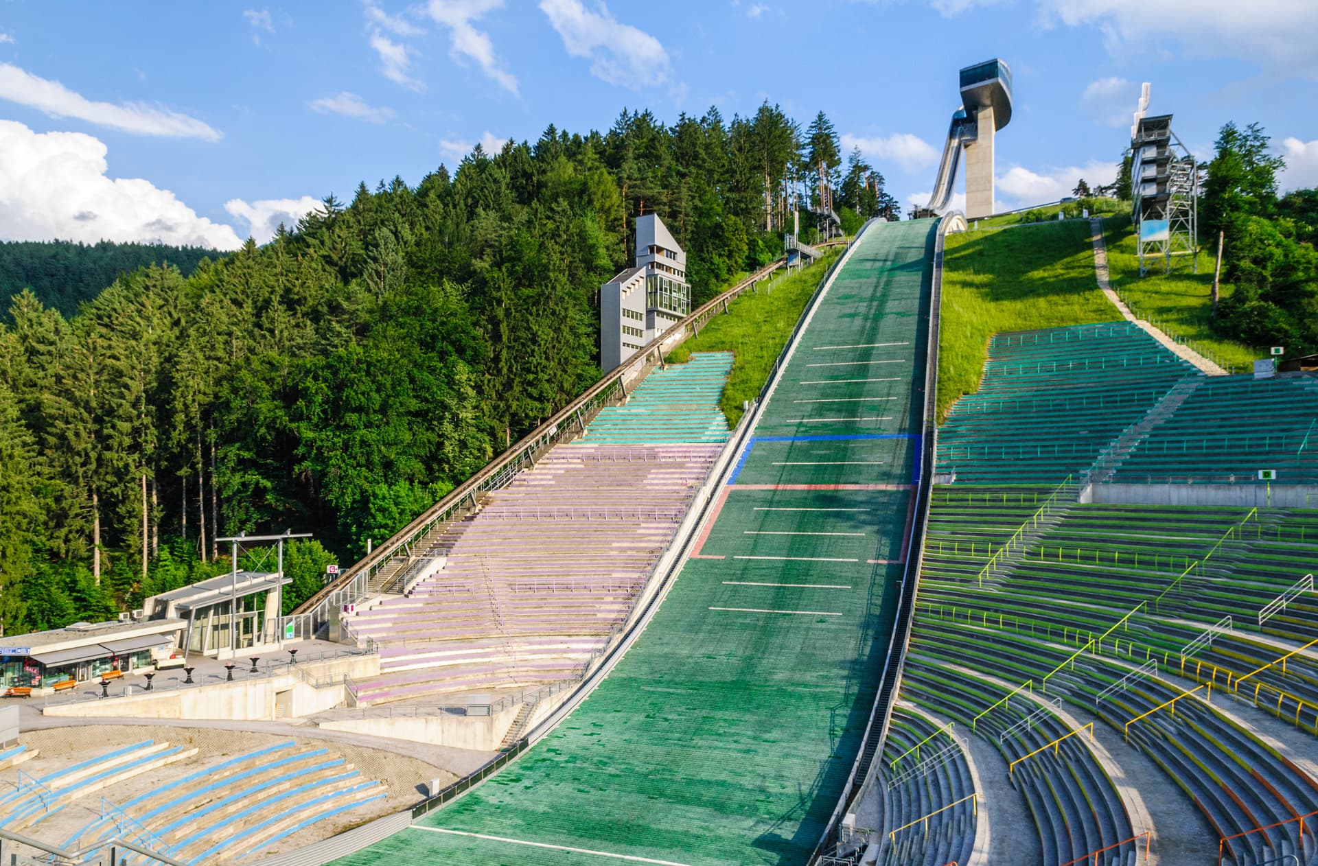 Ski jumping hill with green summer matting and empty stadium seating at Bergisel in Innsbruck.