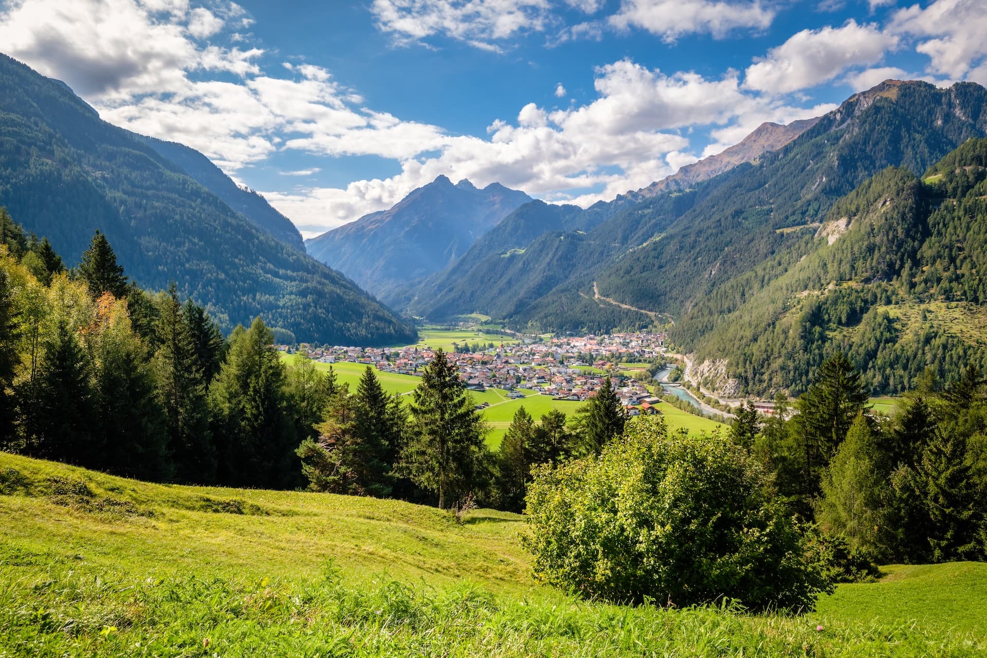 Alpine village nestled in the Inntal Valley, surrounded by steep, forested mountains under a blue sky.