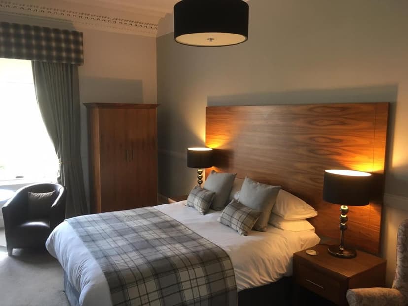 Hotel bedroom with large wooden headboard, plaid throw, and bedside lamps at Ardshiel Hotel.