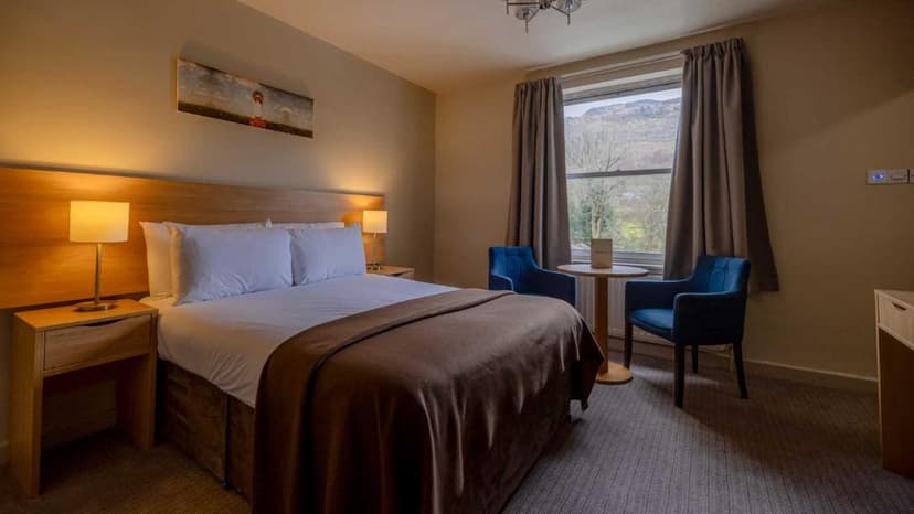 Hotel room with double bed, side tables, and mountain view from window at The Tarbet Hotel.
