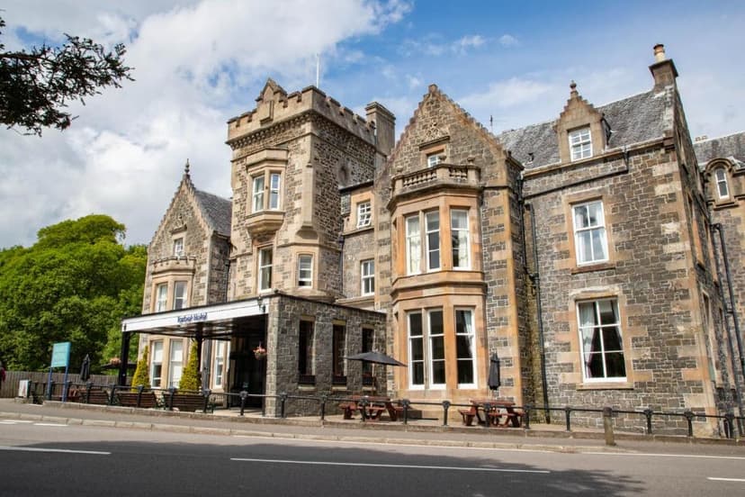 Stone Tarbet Hotel building with outdoor seating area beside a road under a blue sky.