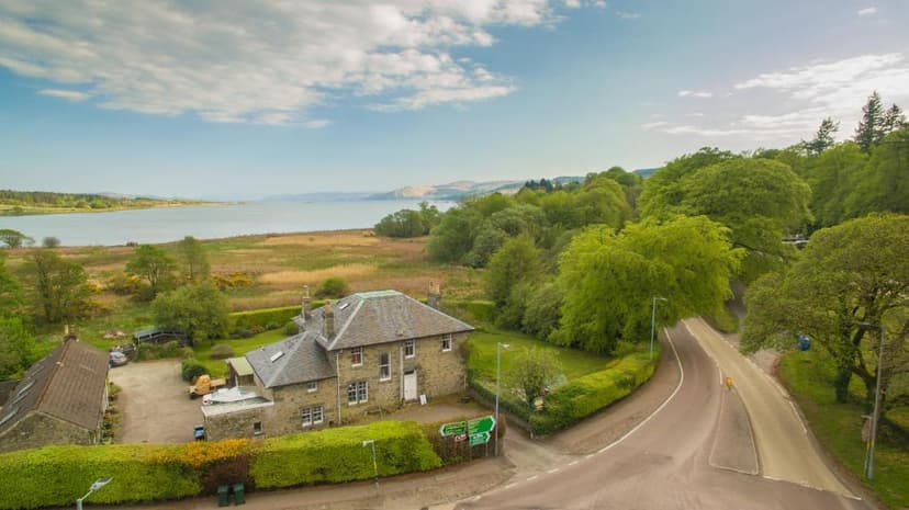 Stone house near estuary with road and lush green trees under blue sky