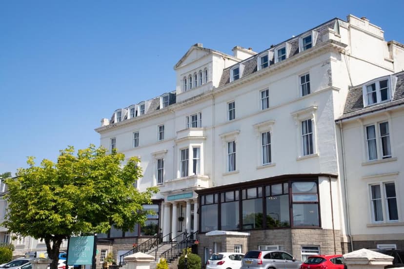 The Great Western Hotel building with white facade, bay windows, and parked cars under a clear blue sky.