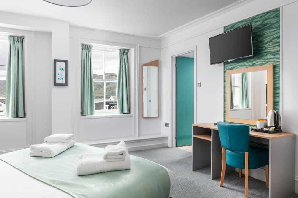 Hotel room with white walls, mint green accents, and view of green hills through windows.