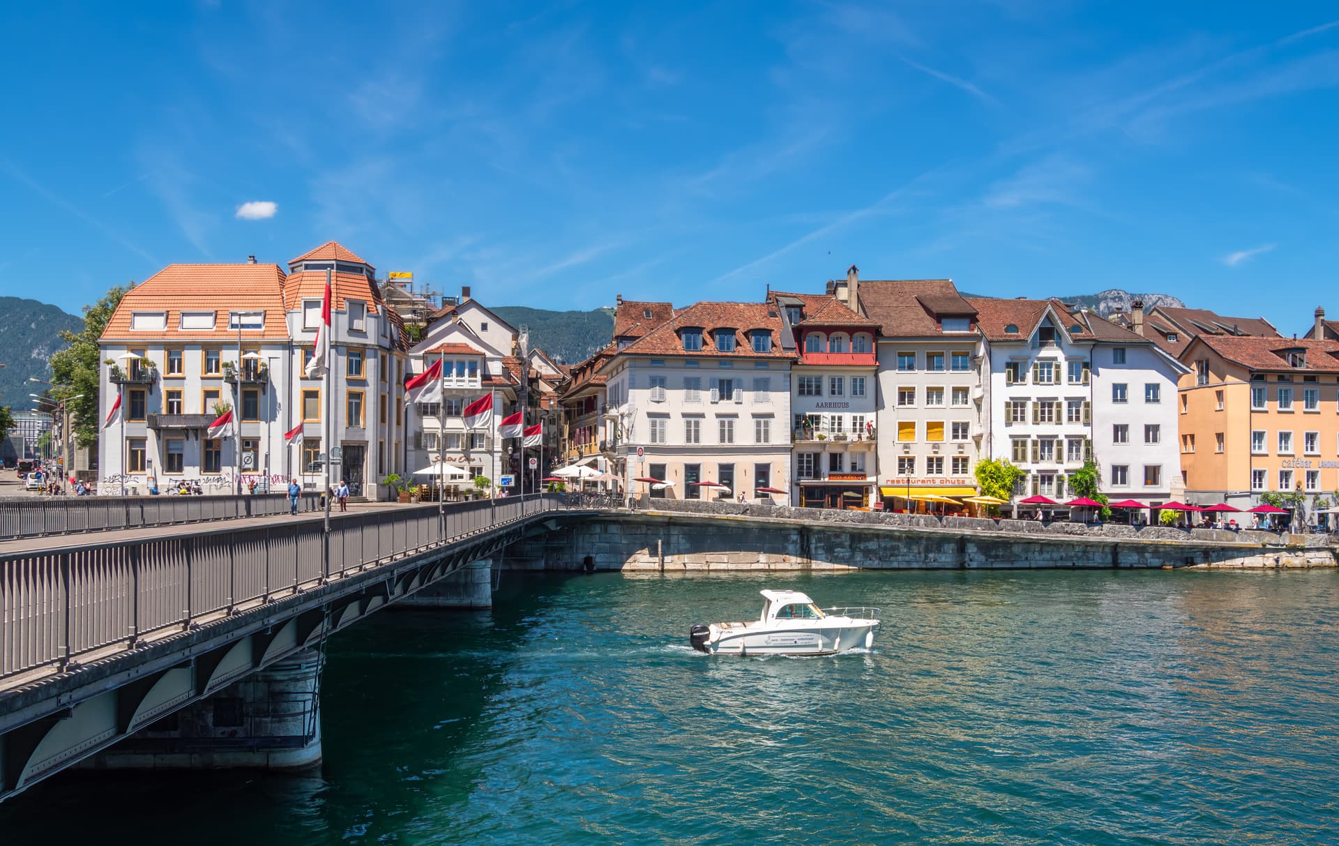 Motorboat on the Aare River under a bridge near historic buildings in Solothurn, Switzerland.