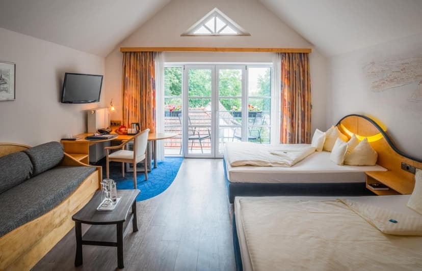 Hotel room interior with twin beds, desk, sofa, and balcony access in Passau.