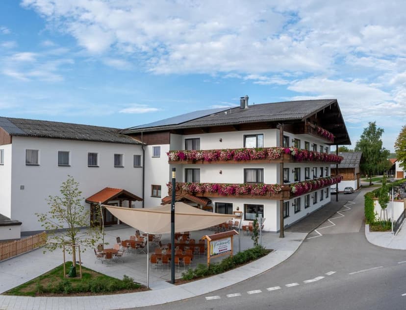 White hotel building with flower boxes, outdoor dining area, and solar panels in Aschach.