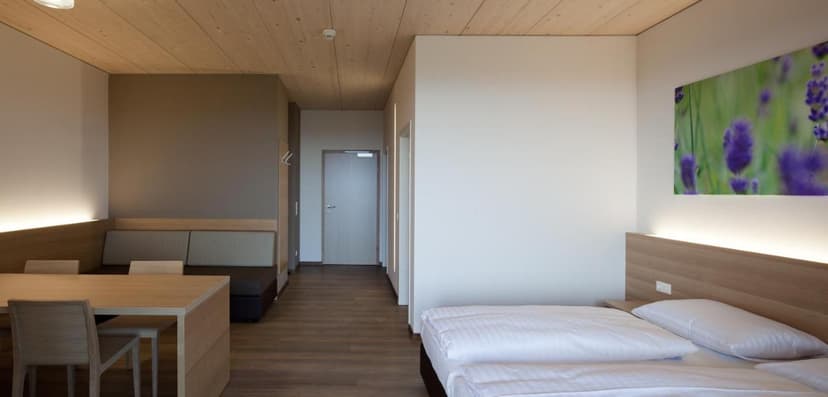 Modern hotel room with wooden ceiling, dining area, and bed, featuring lavender artwork