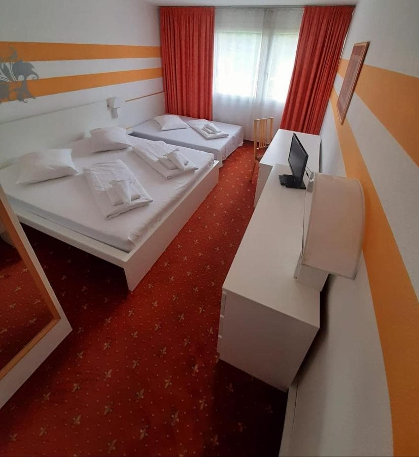 Twin beds in a hotel room with orange striped walls, red patterned carpet, and white furniture in Tulln.