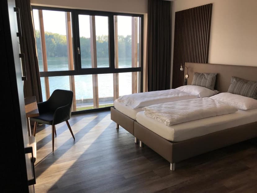 Twin beds in modern hotel room with large window overlooking a river in Enns.